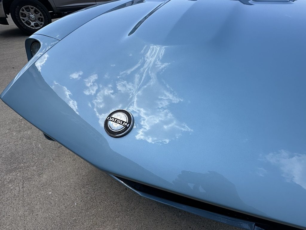 Close-up of the Datsun nose emblem on a deep-gloss light-blue finish