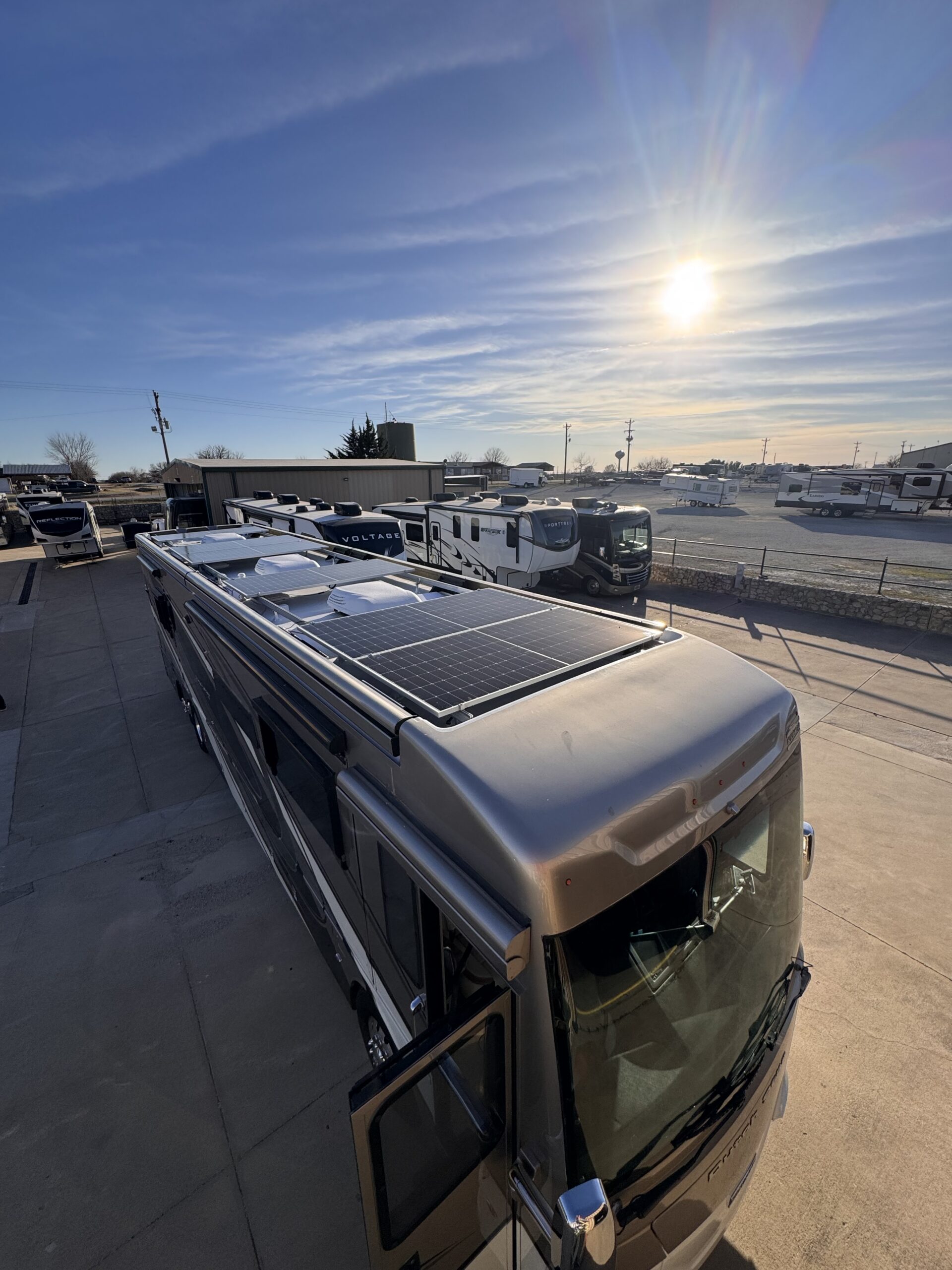 RV with rooftop solar panels at Patriots RV Services lot during sunset